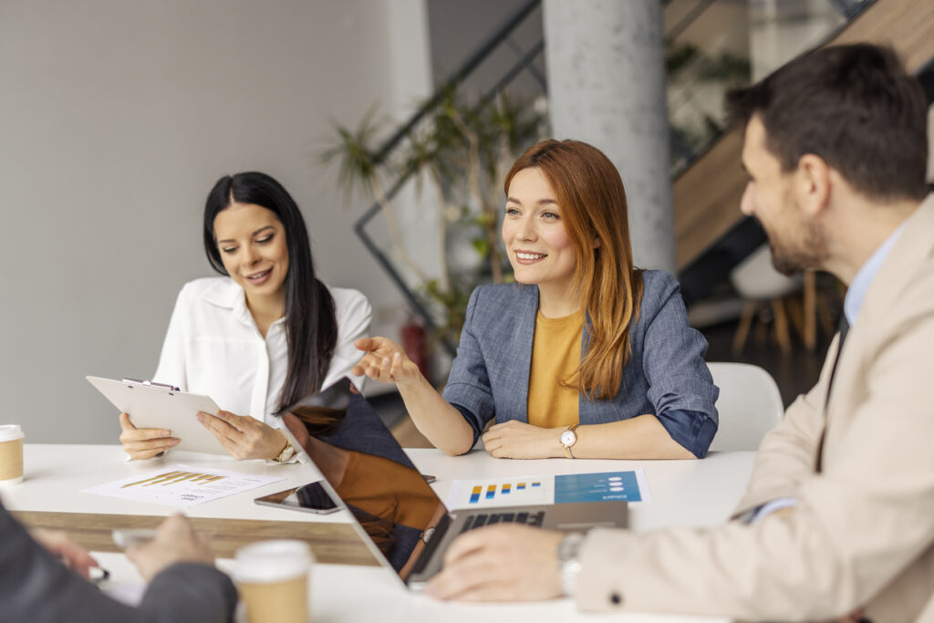 Businesswoman sitting on a meeting at boardroom and discussing analyzes and paperwork with coworkers.