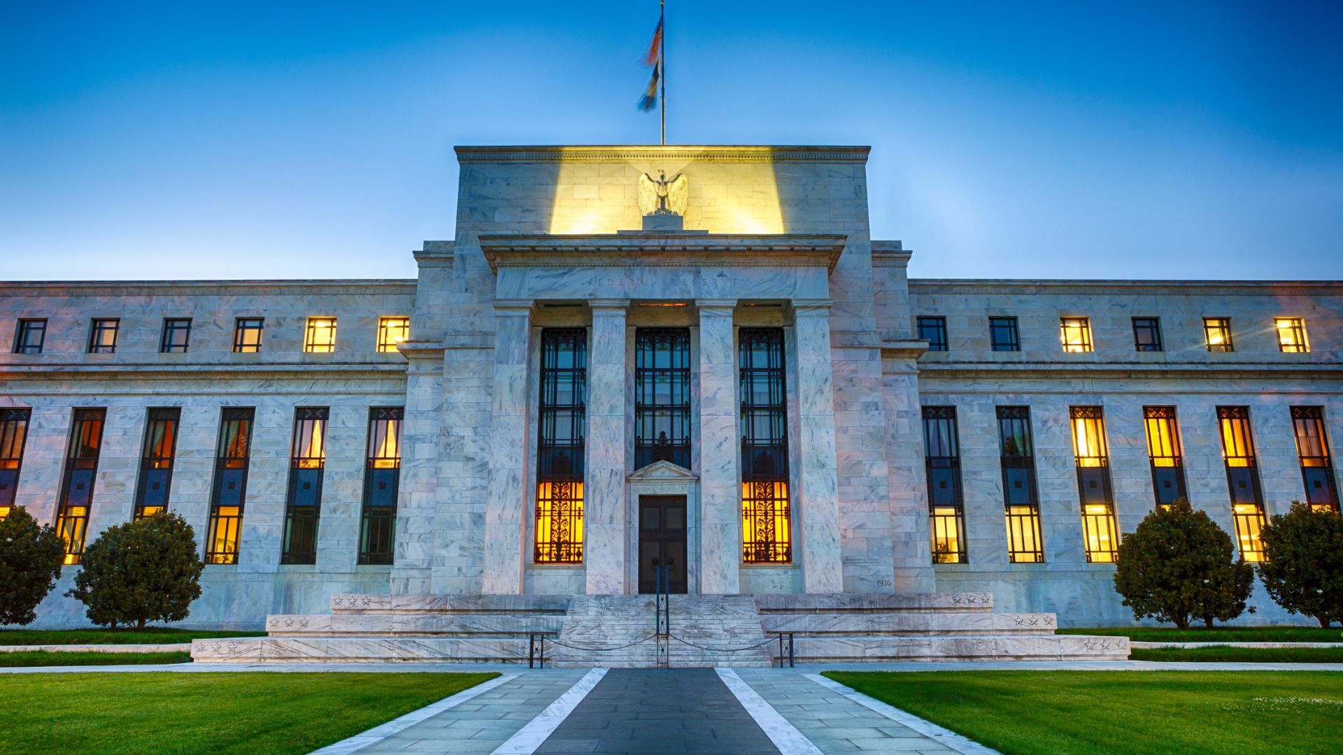 The image shows a grand, illuminated marble building with multiple windows and a central columned entrance. The sky is a rich blue, evoking a formal and majestic tone.